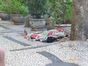 The uneven sidewalks in front of the hotel, along with a sleep homeless Brazilian. 